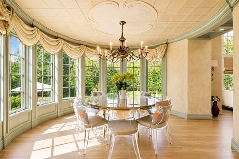 Sunlit dining room with garden views, chandelier, and elegant bay windows