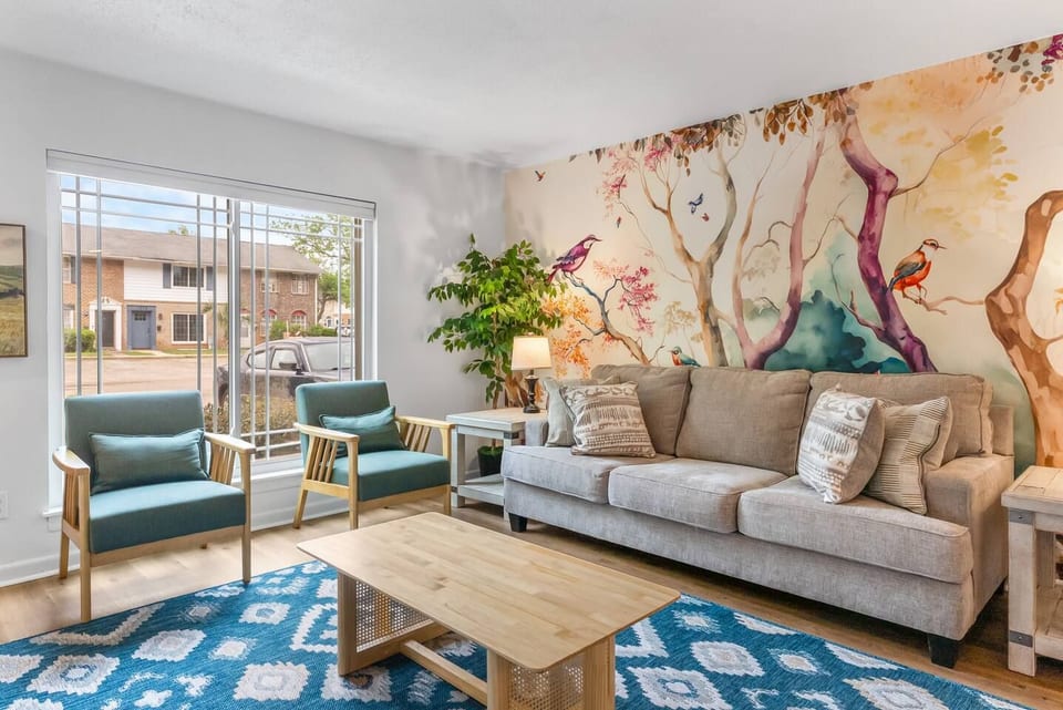Bright living room with bold mural, cozy seating, and natural light
