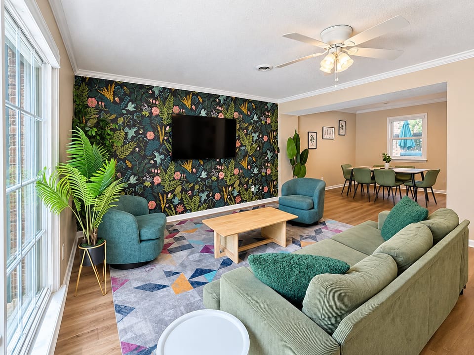 Bright, stylish lounge with botanical wall, TV, and open dining area