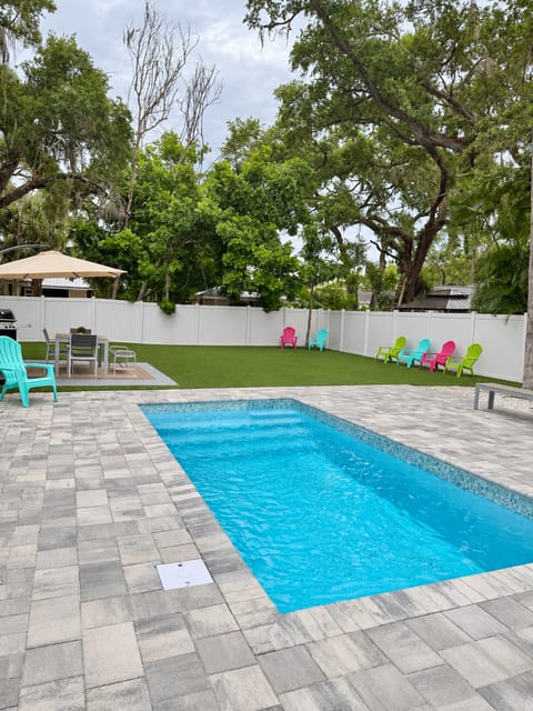 Private heated pool and spacious fenced backyard with artificial turf, colorful seating, and an outdoor dining area.