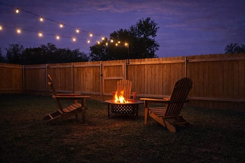 Fire pit glowing under string lights in the fenced backyard