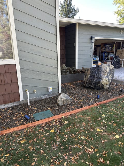 Covered front entry with natural stone landscaping and attached garage