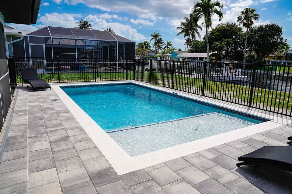 Enjoy year-round swimming in your private heated pool, surrounded by a paved sun deck, secure perimeter fencing, peaceful canal views, and bright blue open sky.