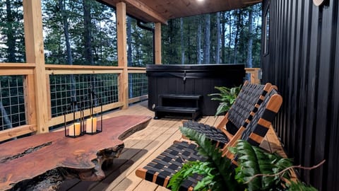 Relax on the covered back deck with a private hot tub, comfortable seating, and a table overlooking the woods.