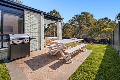 Outdoor Dining Area : Enjoy outdoor dining surrounded by greenery, with a spacious table and BBQ ready for relaxed meals together.