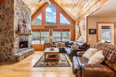 Large open living room with sectional and recliner. This opens to the dining room and kitchen with views out over the field leading to the river.