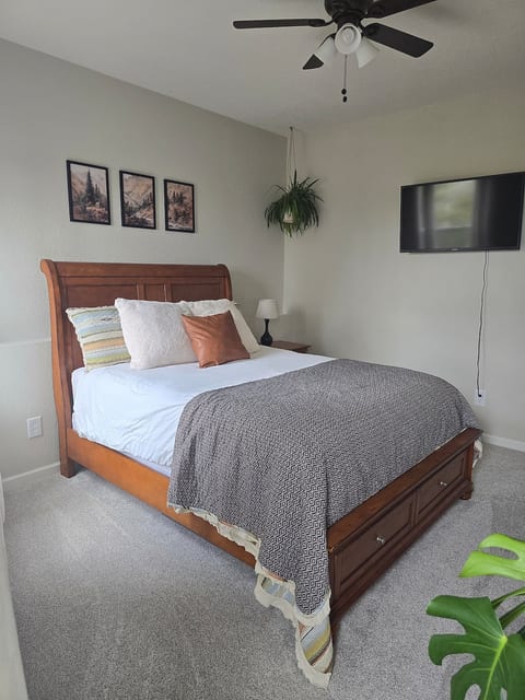 queen bed with smart tv, ceiling fan, extra pillows and dresser storage