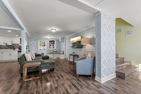 Our cozy open-concept living room features a TV, board games, books, and coastal oyster wallpaper, creating a relaxing space to unwind, watch a movie, read, or enjoy game night with family and friends.