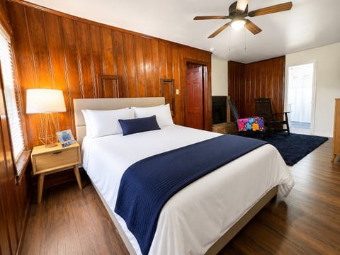 Cozy wood-paneled bedroom with plush bed, seating area, and ceiling fan