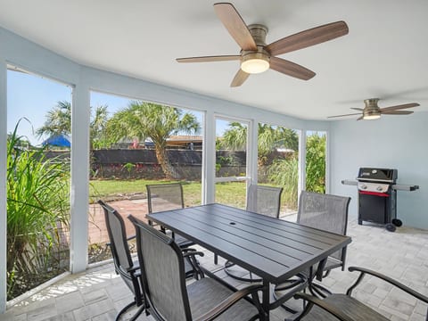 Enjoy outdoor meals and Florida breezes in the screened lanai, featuring a dining table, comfortable seating, and a grill.