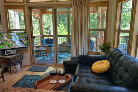 Living room with leather sofa and big windows looking out to the covered patio and forest