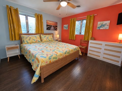 Bright coastal bedroom with colorful decor, hardwood floors, and a king sized bed