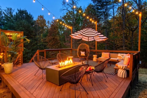 The lower deck at dusk — gas fire pit, string lights, lounge chairs, plush sofa, and an egg chair. This is where your group ends up every evening.