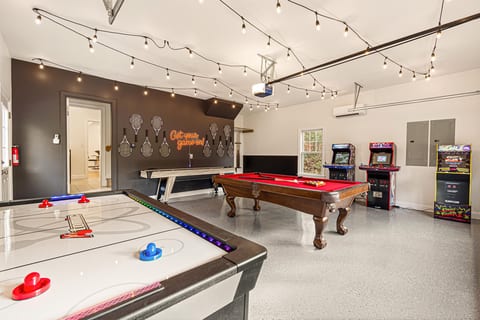 Full view of the game room — air hockey, pool table, shuffleboard, and three full-size arcade cabinets: NBA Jam, Street Fighter II, and NFL Blitz. Climate-controlled and accessible from the main house. Kids will love the chalk wall on the far side.