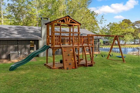Lakeside yard with deluxe playset—swings, slide, and rock wall.