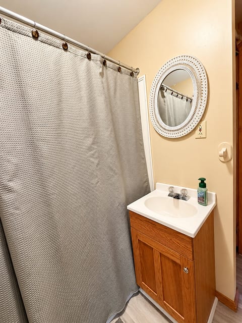 Cozy full bath with shower, wood vanity, and charming round mirror