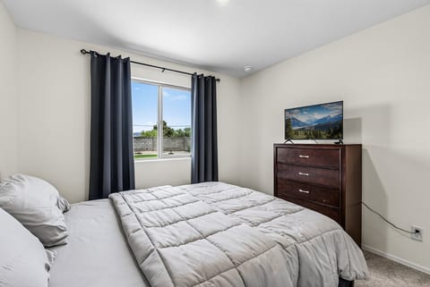 Bright, cozy bedroom with blackout curtains, dresser, and in-room TV