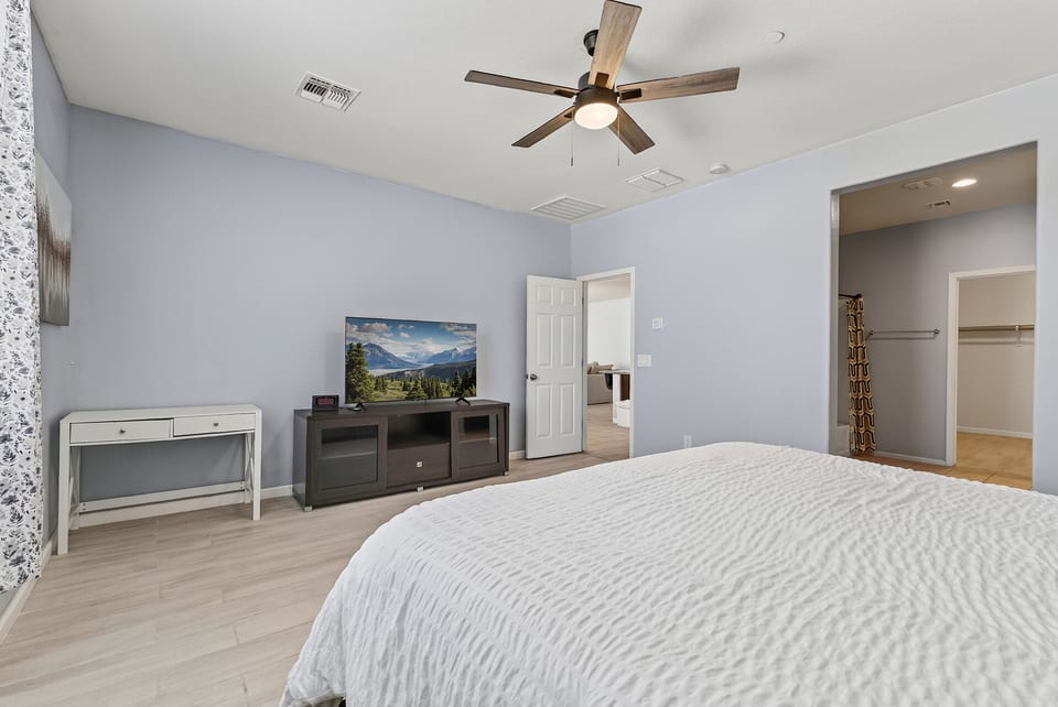 Bright, spacious bedroom with TV, ceiling fan, and walk-in closet