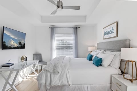 The primary suite with pool and courtyard view, dedicated workspace, large walk in closet, wood hangers, luggage rack, dresser, and 55" tV