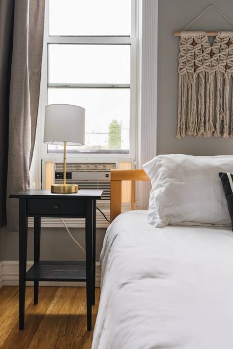 Master Bedroom - left side of bed with AC unit, nightstand, and table lamp with charging outlet at base.