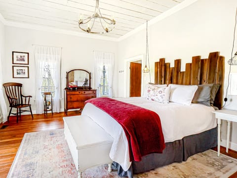 Primary bedroom with the original flooring, ceiling, and windows of the schoolhouse.