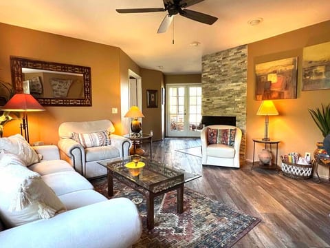 Large open living area with large sofa bed and oversized chair, copper accent tables, wood burning fireplace, and updated flooring.