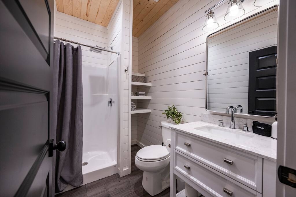 Modern guest upstairs bathroom with glass shower, marble vanity, and stylish open shelving.