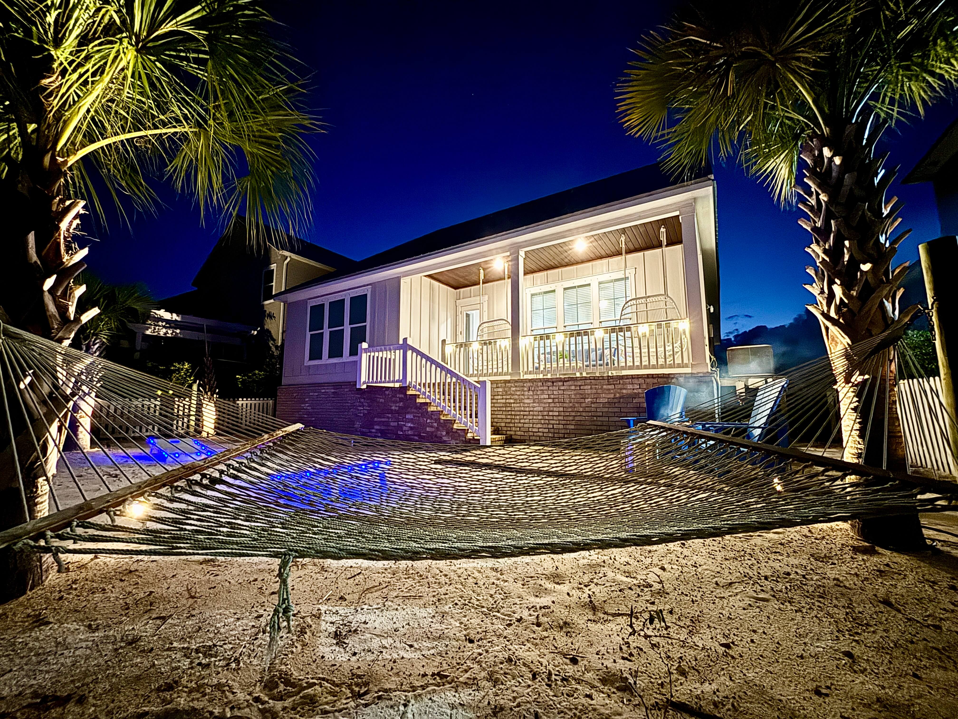 Lounge by twilight: hammock sways, palm silhouettes, and beach house glow for dreamy vibes.