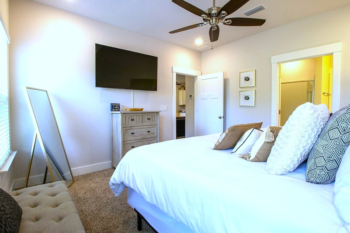 Bright bedroom with king bed, TV, ceiling fan, and ensuite bath.