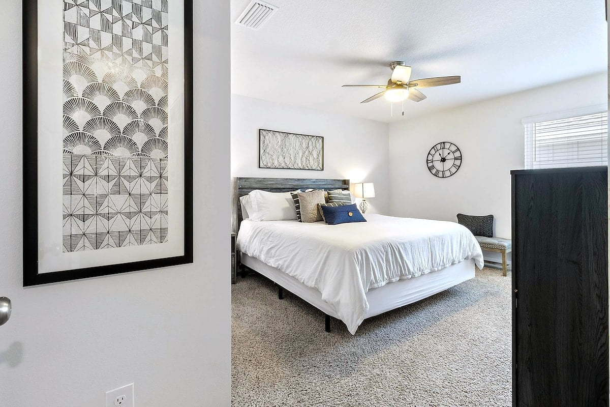 Serene king bedroom with natural light, ceiling fan, and plush carpet.