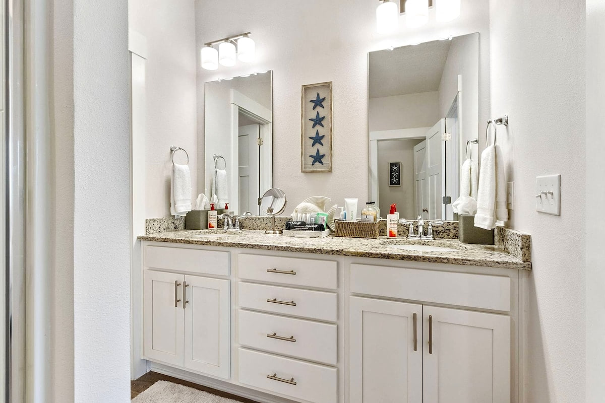 Bright double-vanity bath with granite counters, twin mirrors, and plush towels