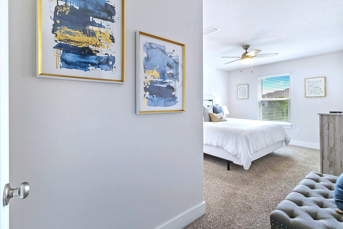 Sunny, serene bedroom with luxe linens, ceiling fan, and chic art.