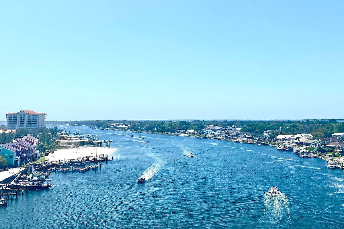 Panoramic bayview: boats, sandy shoreline, docks, and sunshine.