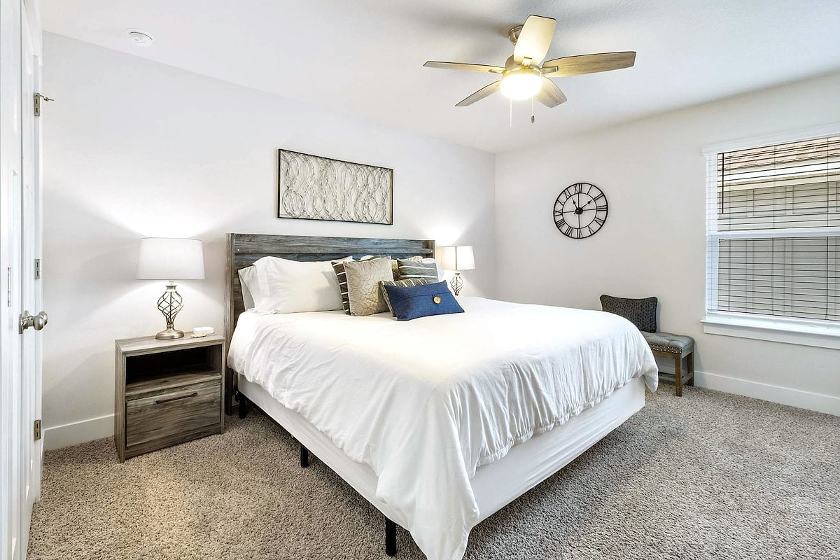 Bright king bedroom with plush carpet, ceiling fan, and ample natural light.