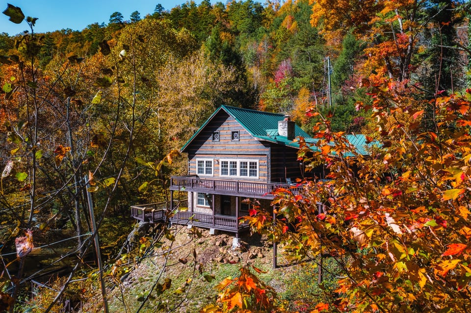 Charming cabin peeking through a canopy of brilliant autumn leaves — your private fall retreat.