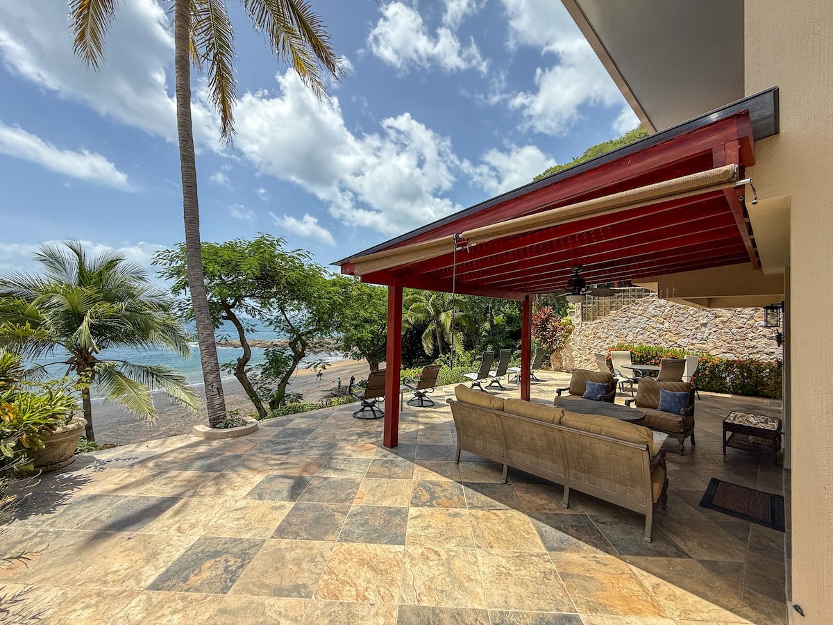 Cushioned seating under a pergola, surrounded by tropical palms and ocean breeze—an ideal space for relaxed gatherings, shaded reading, or cocktails with a view.