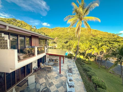 Expansive stone-tiled patio with cushioned lounge chairs, shaded dining, and lush garden views—ideal for sunrise coffee, sunset gatherings, or simply soaking in the coastal breeze.
