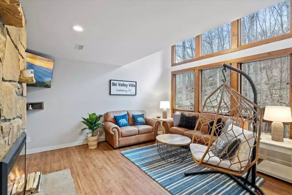 Comfortable living room with large floor to ceiling windows, comfortable couches, smart tv with cable and electric fireplace.