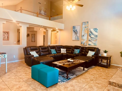 Relax in the spacious, sunlit living room featuring a plush leather sectional, designer accents, vaulted ceilings, and a stylish, open layout perfect for family gatherings or work breaks.