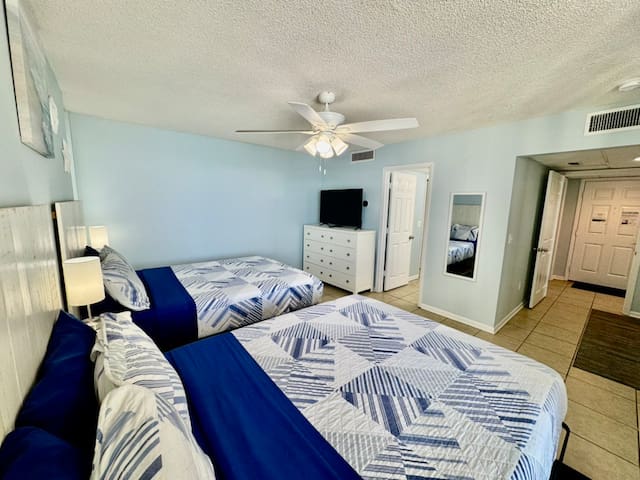 Rear bedroom with two queen beds and private full bath. Unit entry door just beyond bedroom door on the right