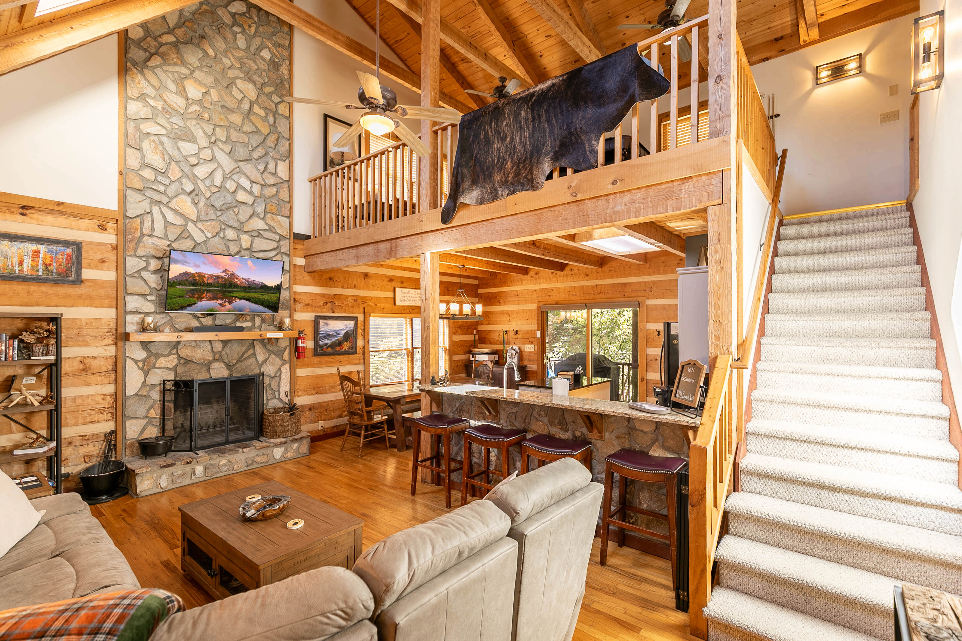 Main level common area and staircase to the loft area. Sectional has three recliners, family games are located in the coffee table, kitchen table seats eight, and four bar stools at the bar. Bookshelf has several classics ready to enjoy!