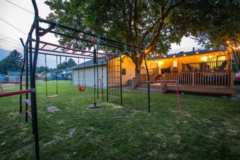 Spacious backyard with playset, lawn, and a glowing deck under the trees
