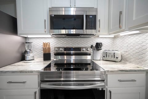 A modern kitchen with white cabinets, stainless appliances, and a sleek fish-scale backsplash for elegance.