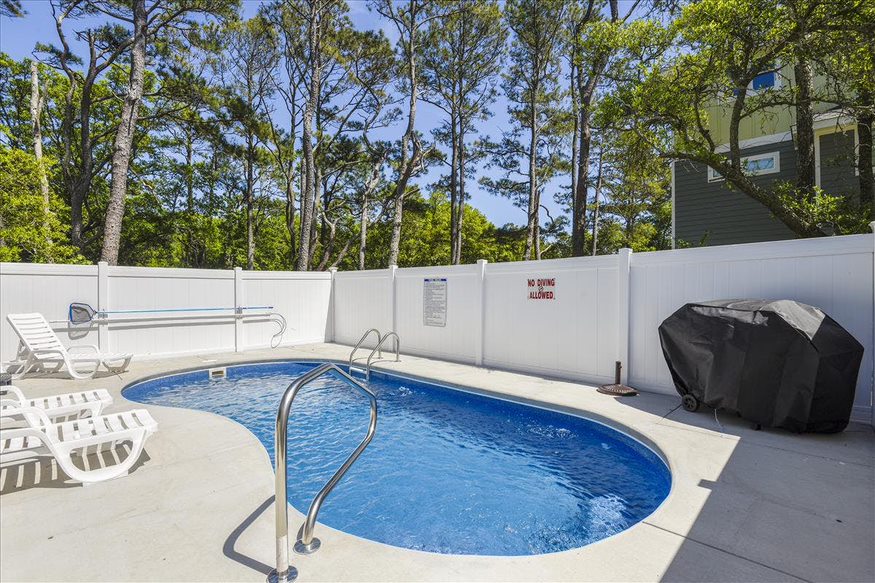 A charming poolside retreat with seating and a lush tree-lined backdrop.