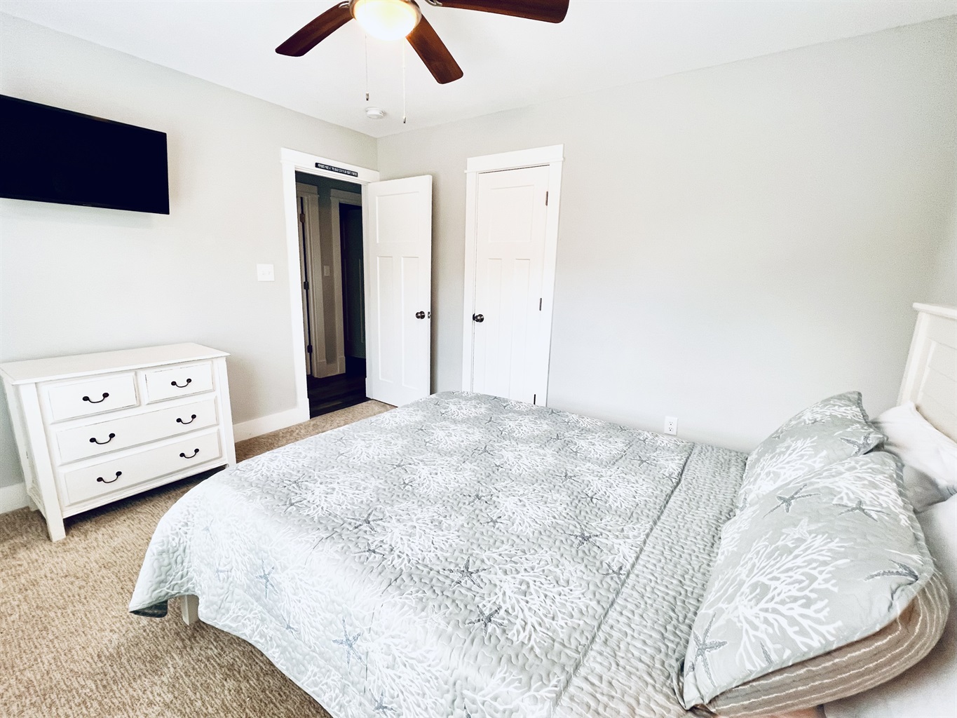 Experience a serene bedroom with a comfortable bed, soft carpeted floors, and a spacious dresser, all under the gentle sunlight streaming through the window.
