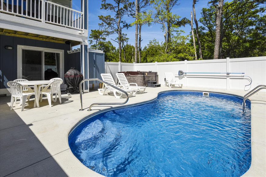A cozy pool area with a small pool, a seating area, and a picturesque backdrop of surrounding trees.