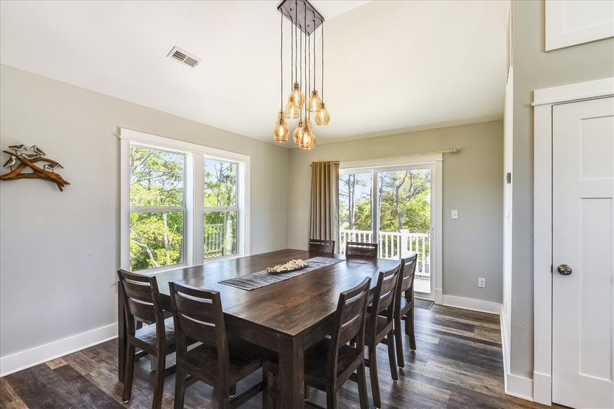 A chic dining area with an elegant chandelier, offering a view of the deck through sunlit windows.