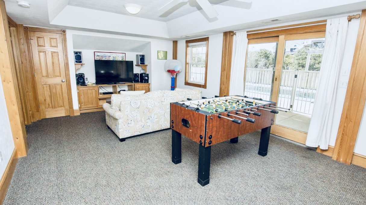 Entertainment room with a foosball table, comfy sofa, and TV on a carpeted floor.