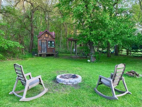 View of the fire pit, tiny house, gazebo and hammocks hanging from the trees. During the summer it’s like a wonderland when all the trees have their leaves. Our property is fenced with some split rail and solid 6’ panels.