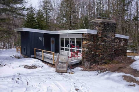 Present day Kilbourne Lodge. A mid-century angled roof ski chalet with large accent stone wall. Front deck features a vintage 2-seater ski lift chair painted in bright red. 100% Instagram worthy!